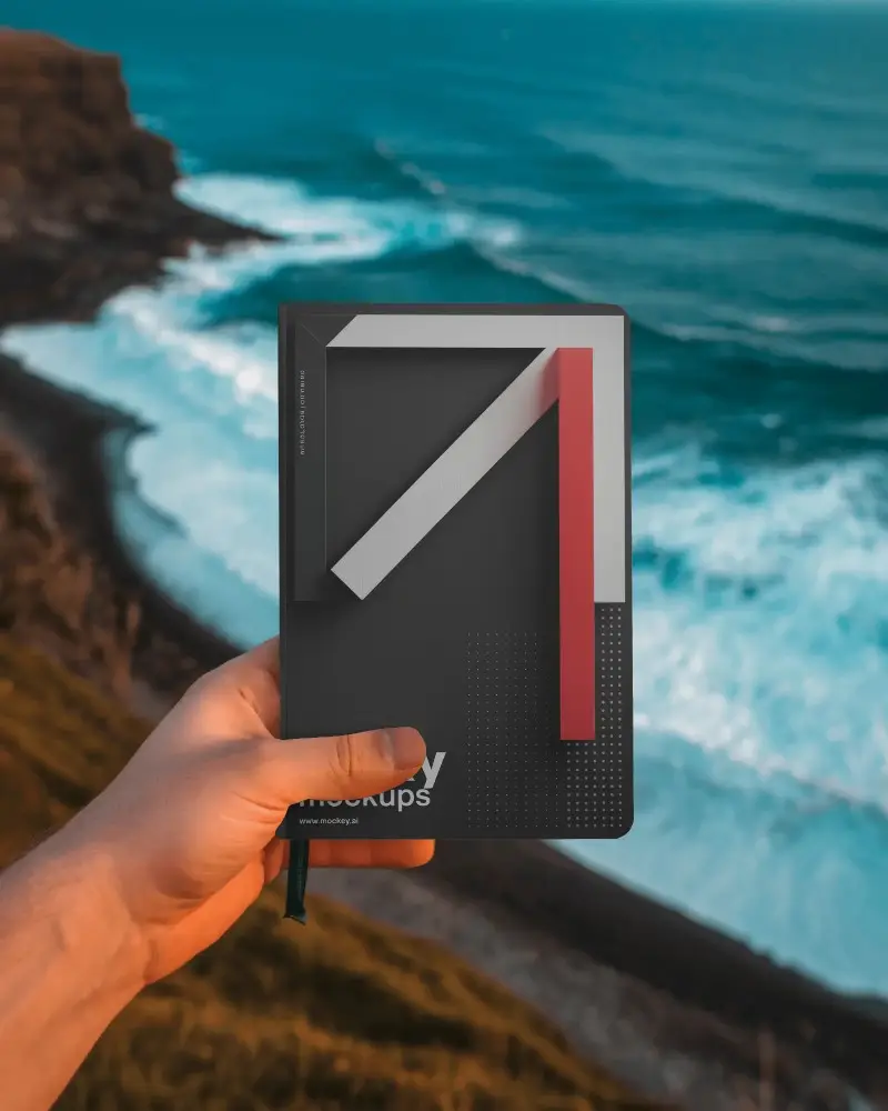 Ocean Cliff Notebook Mockup Held Out Over Crashing Waves And Scenic Coastal View