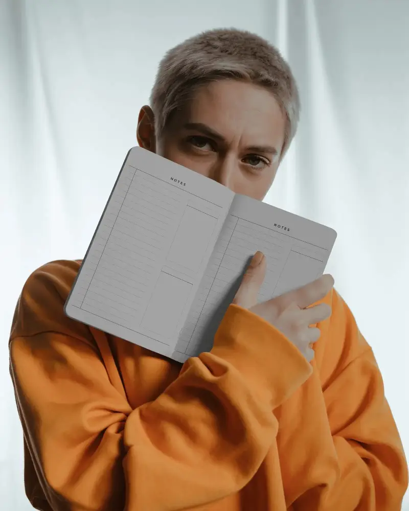 Open Notebook Mockup Held Close By Model In Orange Sweatshirt With Soft Studio Lighting