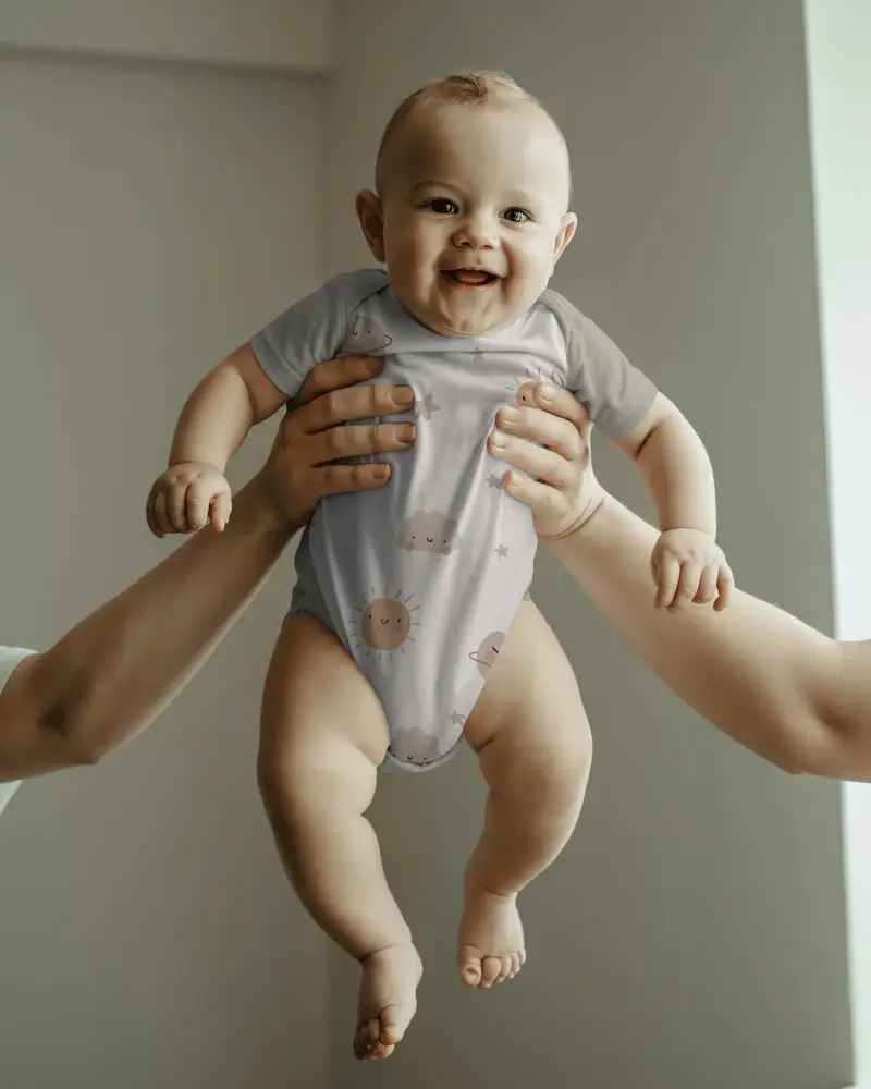 Cute Infant Giggling In Plain Baby Mockup Onesie Held Up With Neutral Background