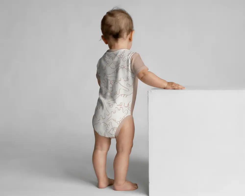 Angled Back Onesie Mockup Toddler Standing Beside White Cube With Clean Background Setup