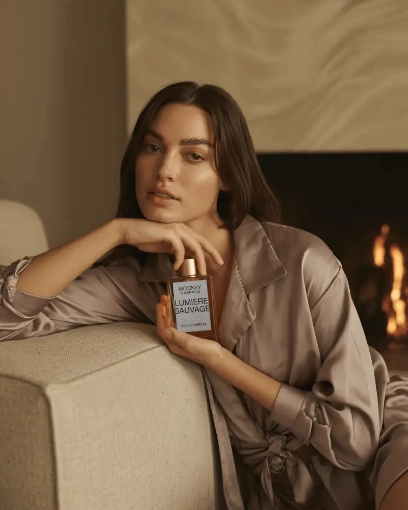 Cozy Luxury Perfume Mockup Female Model In Satin Near Fireplace Holding Bottle