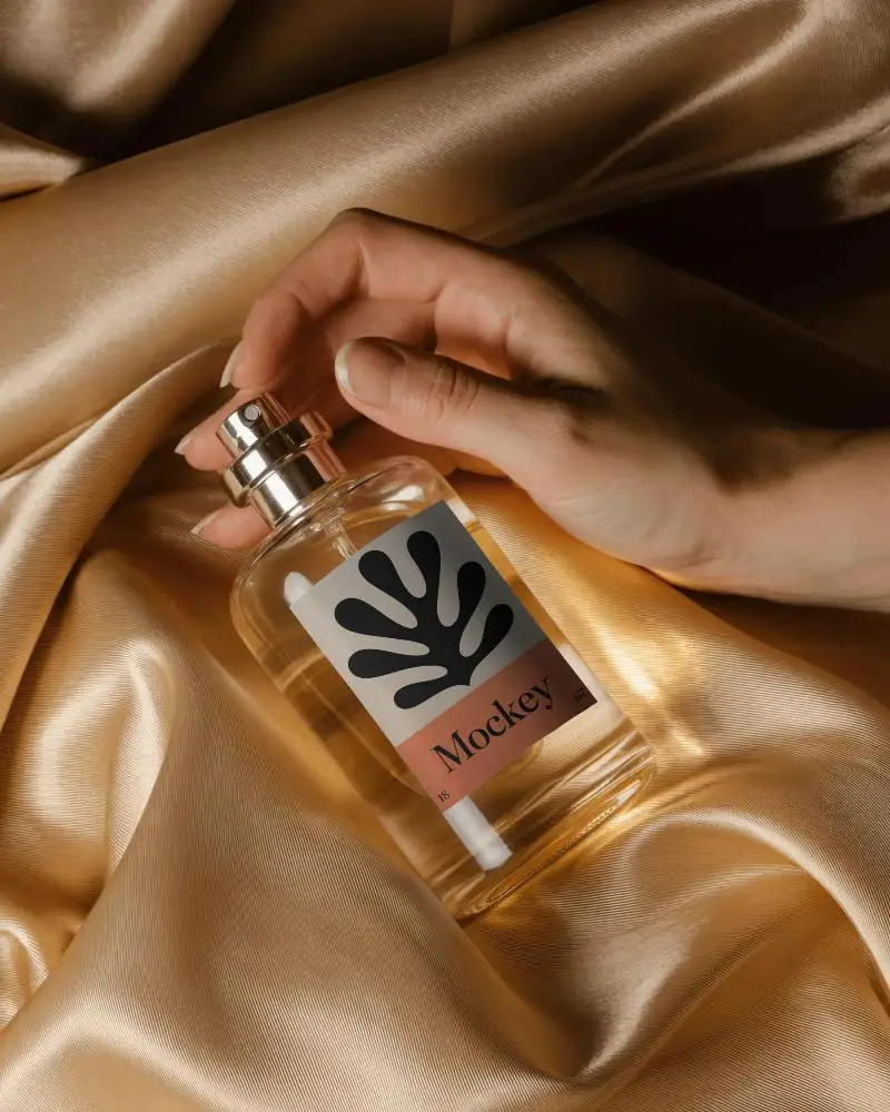 artistic-perfume-mockup-hand-gripping-clear-glass-bottle-on-luxury-golden-fabric-soft-lighting