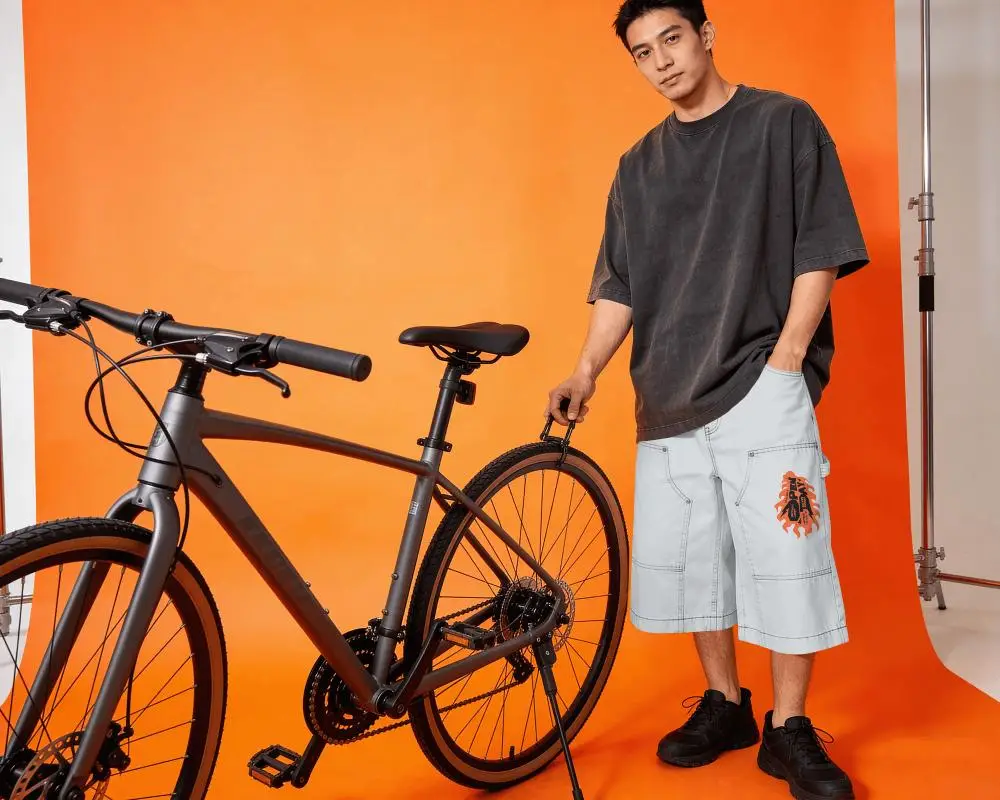 Studio Bike Shorts Mockup Male Model Standing With Bicycle Bold Orange Backdrop Strong Contrast
