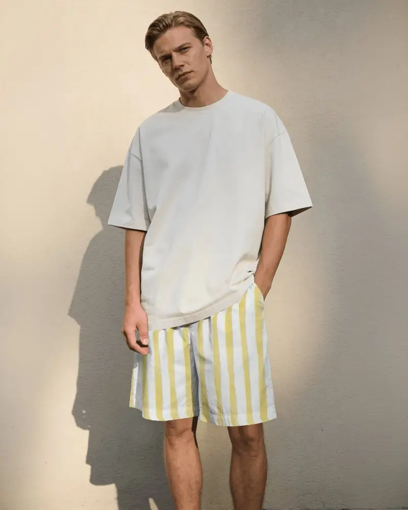 Sunlit Wall Shorts Mockup Male Model Standing With Hand In Pocket Strong Natural Shadow
