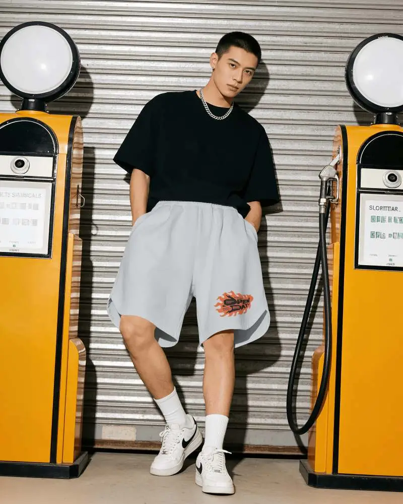 Streetwear Shorts Mockup Male Model Leaning Between Vintage Gas Pumps With Urban Garage Background