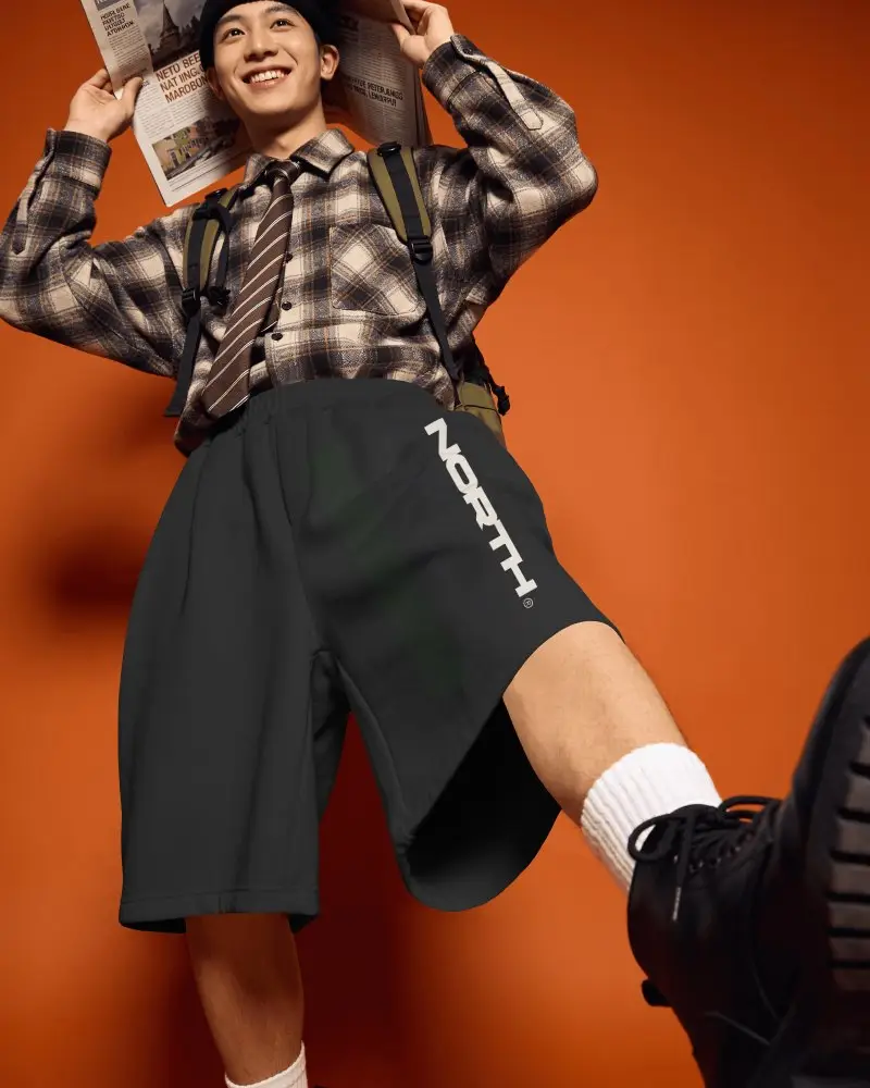 Low Angle Streetwear Shorts Mockup Male Model Posing With Newspaper Against Bold Orange Studio