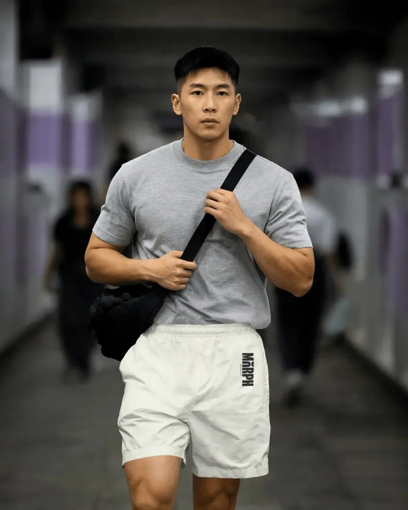 Realistic Sports Shorts Mockup On Male Model With Crossbody Bag And Blurred Hallway Background