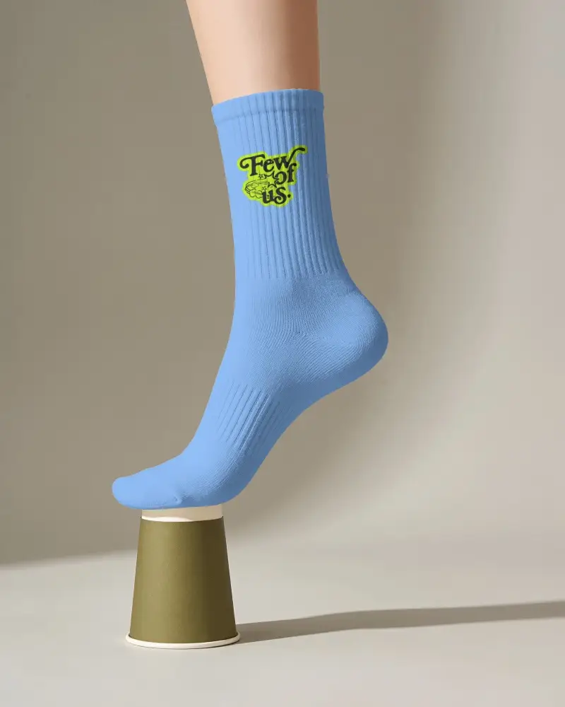 Single Crew Sock Mockup With Model Balancing Toe On Small Cup Pedestal In Minimal Studio