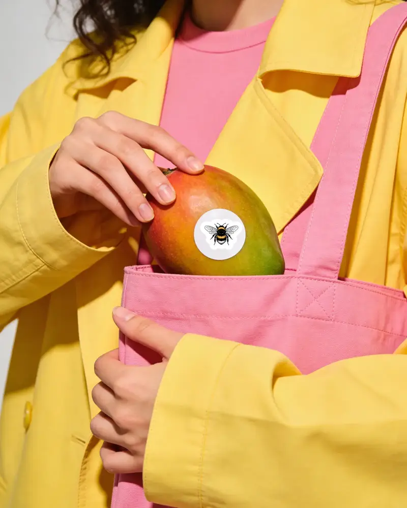 Person Holding Mango With Blank Round Sticker On Fruit In Tote Bag For Custom Branding