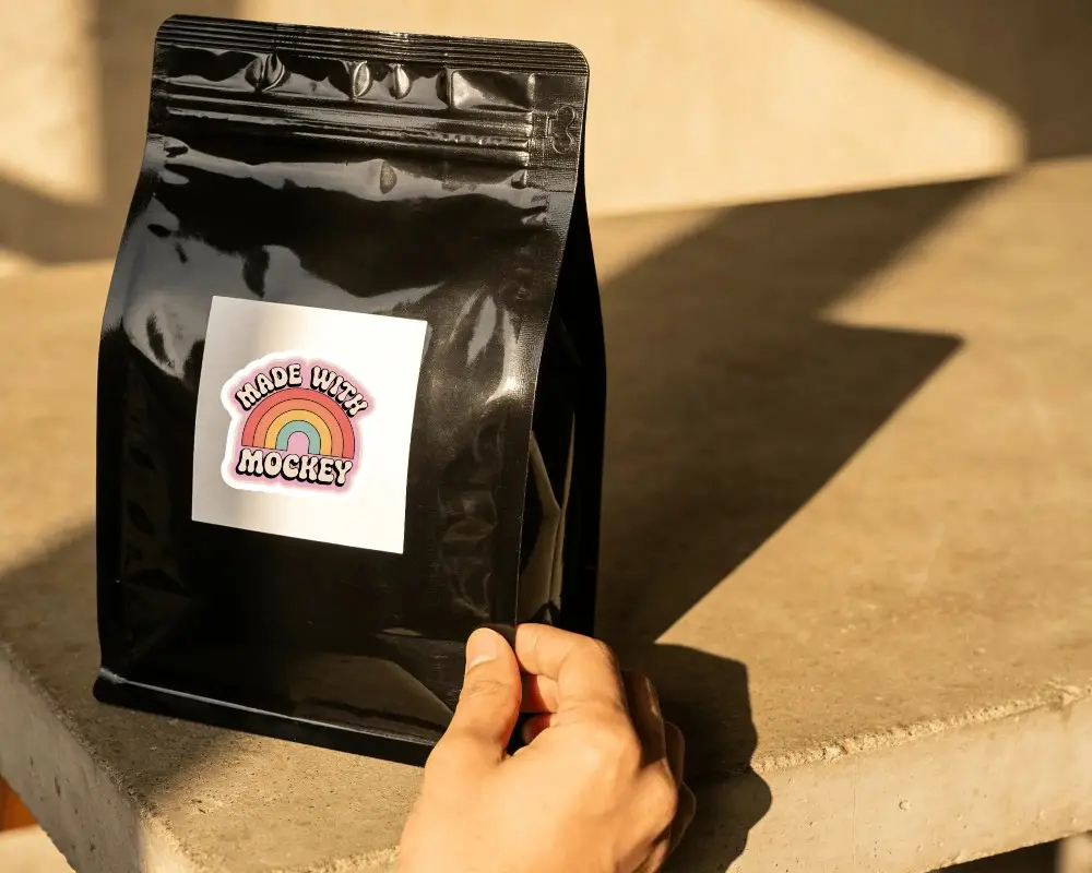 Hand Holding Stand Up Pouch With Square Sticker Label Mockup For Product Packaging Display