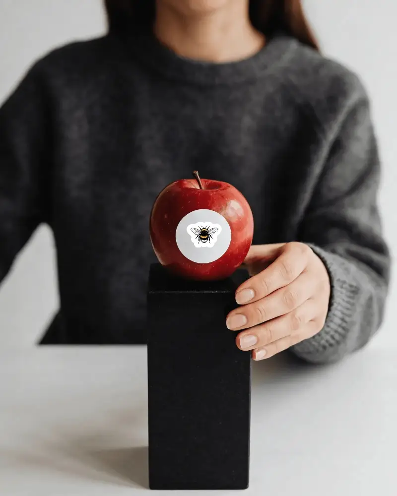 Realistic Fruit Sticker Mockup With Circular Label Held By Hand On Black Pedestal Display