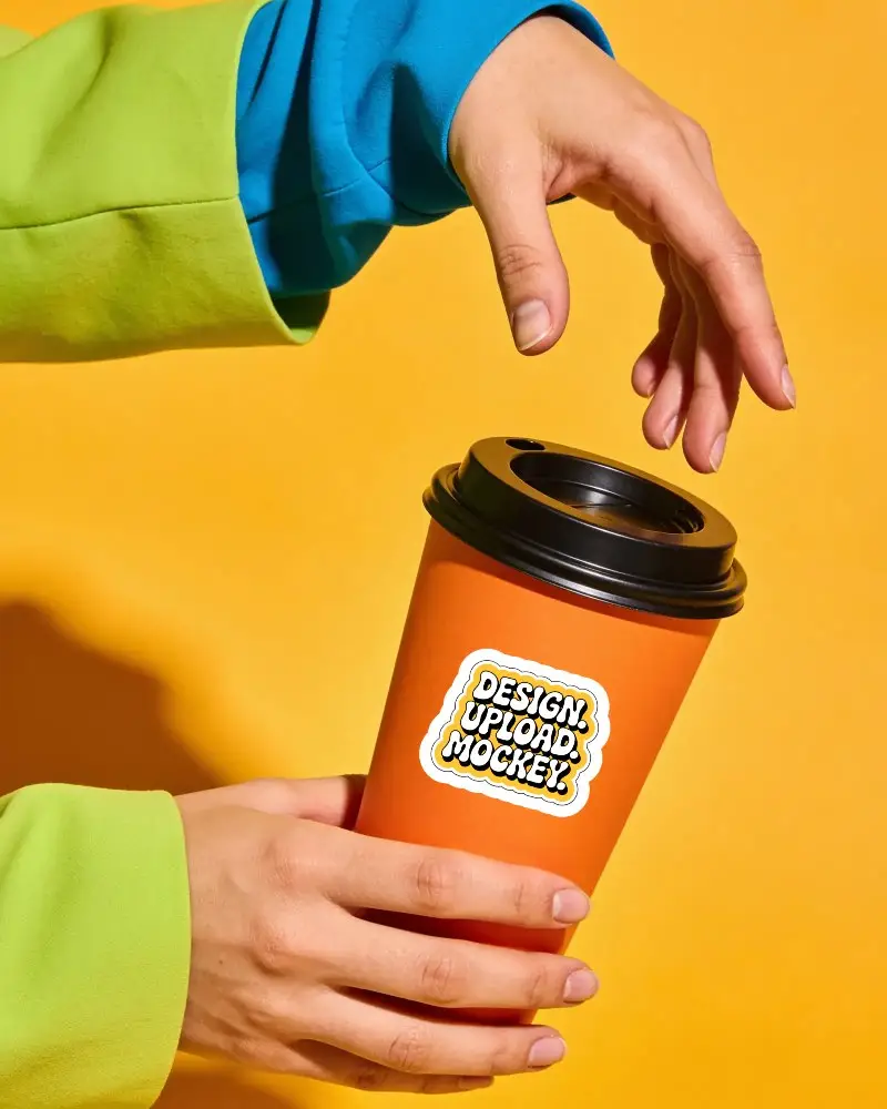 Id Bright Orange Coffee Cup Sticker Mockup Held By Hands Against Yellow Background