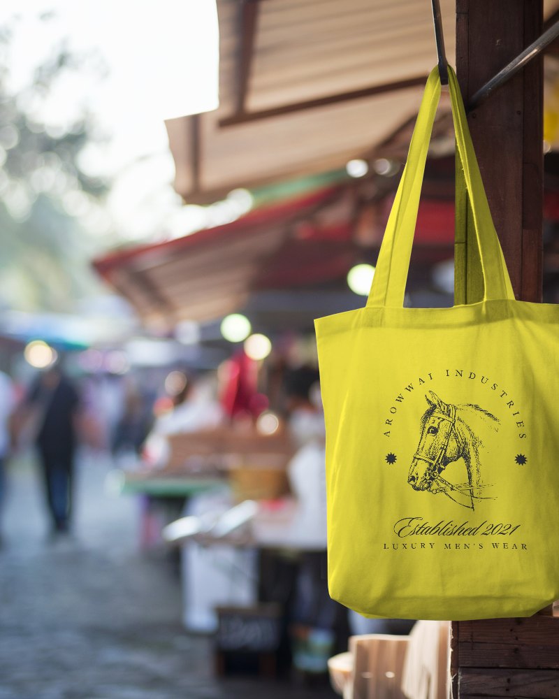 Outdoor Market Tote Bag Mockup White Canvas Tote Hanging On Wooden Post In Busy Daytime Market Blurred Background 0129