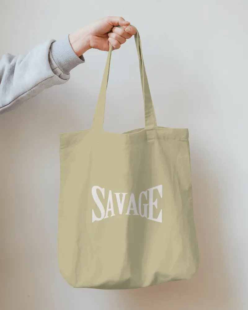 Neutral Wall Totebag Mockup Hand Holding Light Olive Bag Minimal Statement Design Savage Text In Bold Distorted Serif Font Casual And Edgy Aesthetic
