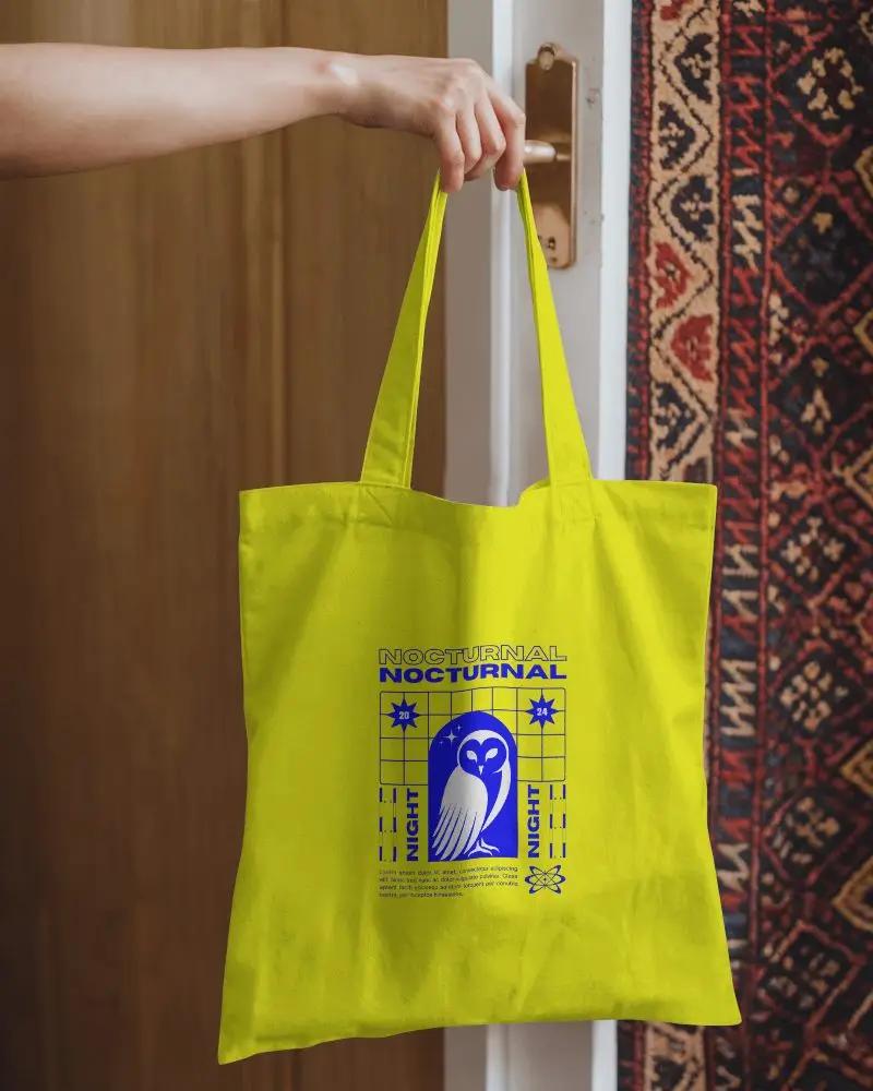 Entryway Totebag Mockup Held By A Hand In Front Of A Door With A Richly Patterned Rug And Warm Tones Cozy And Inviting Ambience