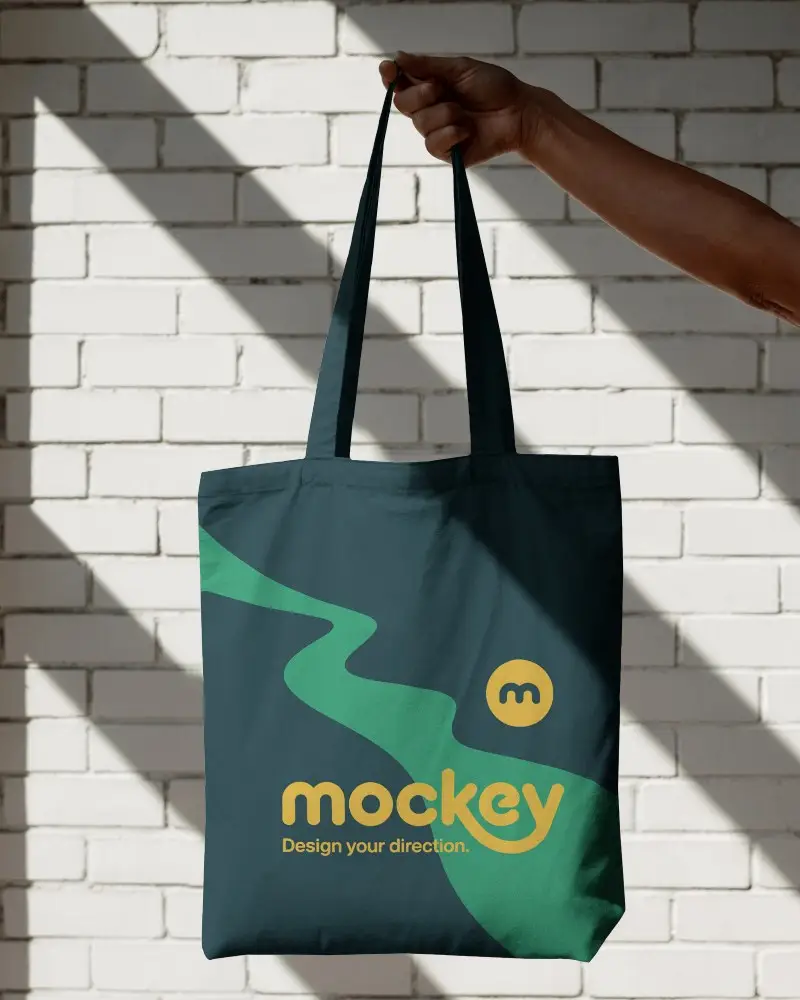 Hand Holding Tote Bag Mockup In Sunlit White Brick Wall Background Contrasting Light And Shadows