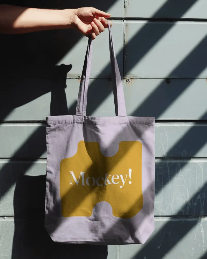 Hand Holding Tote Bag Mockup With Angled Shadows On Light Blue Panel Wall Modern Urban Aesthetic