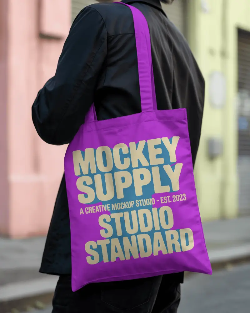 Tote Bag Mockup Over Shoulder On Street With Colorful Building Background