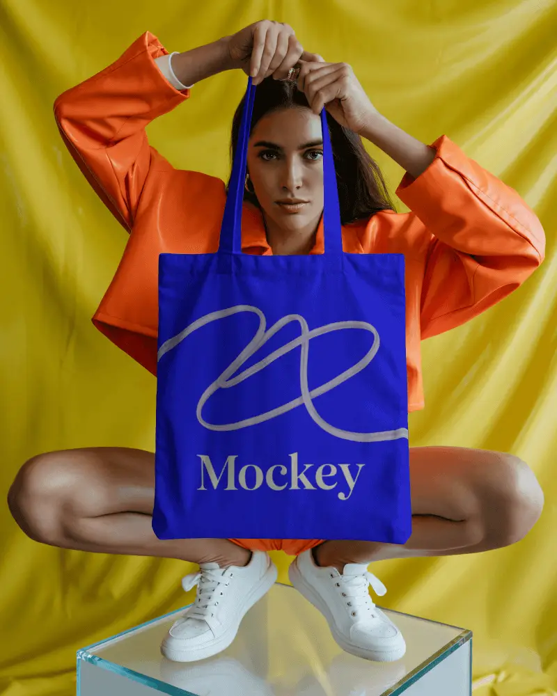 Bold Fashion Tote Bag Mockup Model Posing Against Yellow Backdrop In Orange Jacket Studio Vibe