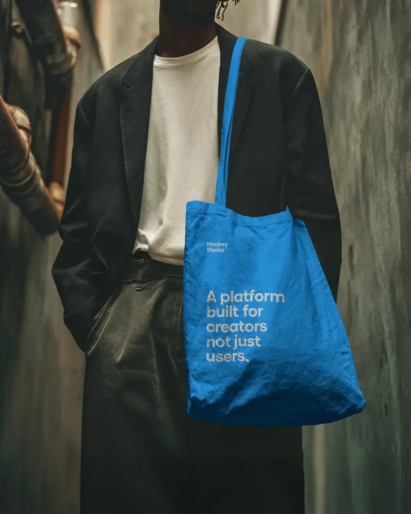 Urban Fashion Tote Bag Mockup Male Model Carrying Canvas Bag In Moody City Alley