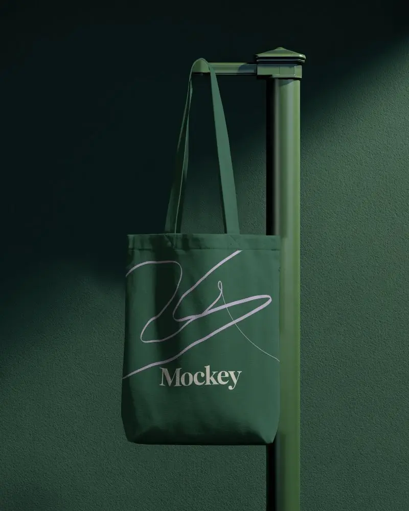 Vertical Post Totebag Mockup Hanging On Minimal Green Stand With Soft Directional Light