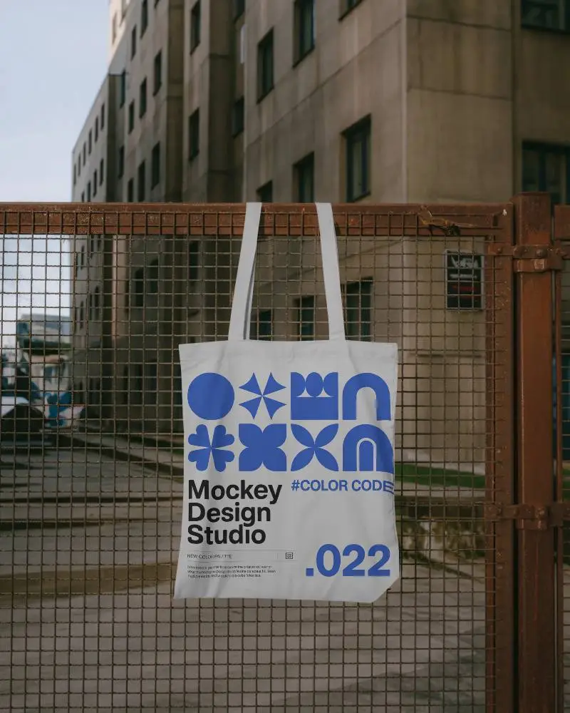 Minimalist Stylish Tote Bag Mockup Hanging On Rustic Metal Fence In Urban Setting