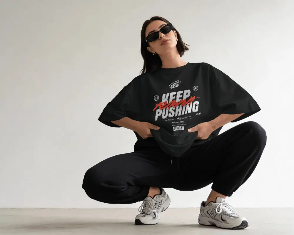 Edgy Streetwear T Shirt Mockup Female Model Squatting Pose Sunglasses Minimal Studio Background