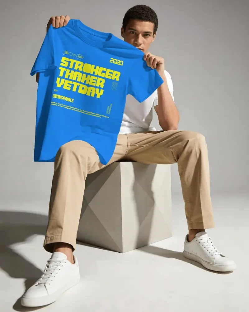 Hand Held T Shirt Mockup Male Model Sitting On Cube Presenting Shirt Clean Studio