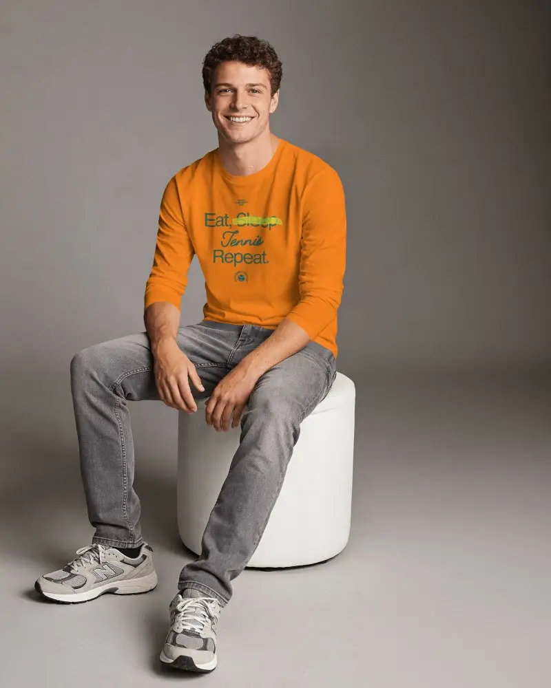 Studio Seated T Shirt Mockup Male Model On Cylindrical Stool Relaxed Smile Clean Background