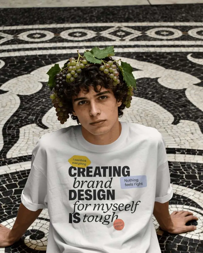 Artistic T Shirt Mockup Male Model Sitting On Decorative Mosaic Floor With Grape Crown Styling