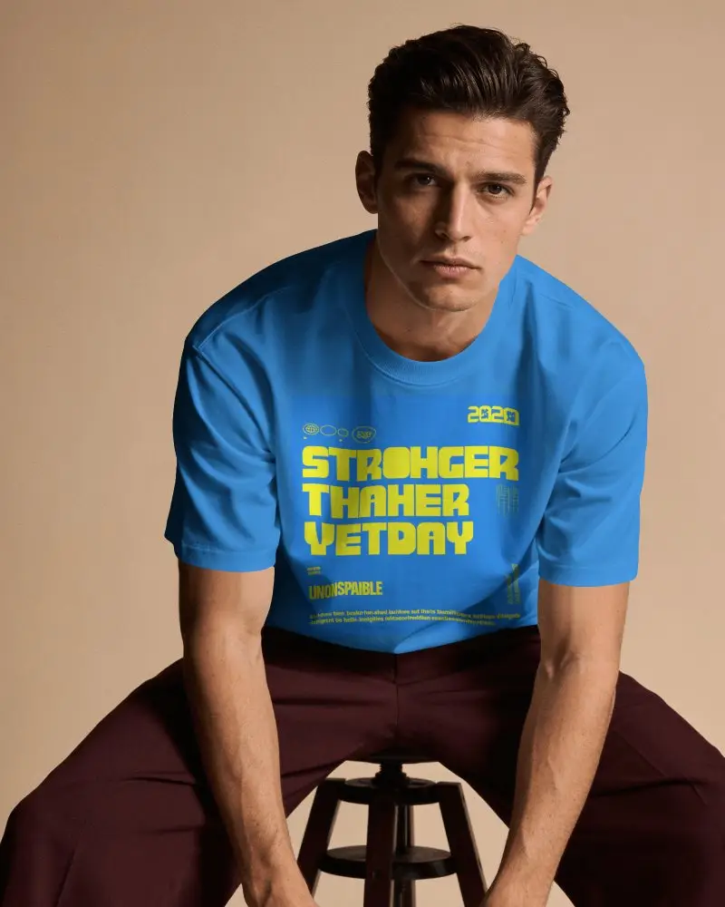 Mens T Shirt Mockup Male Model Sitting On Stool Against Warm Beige Studio Background