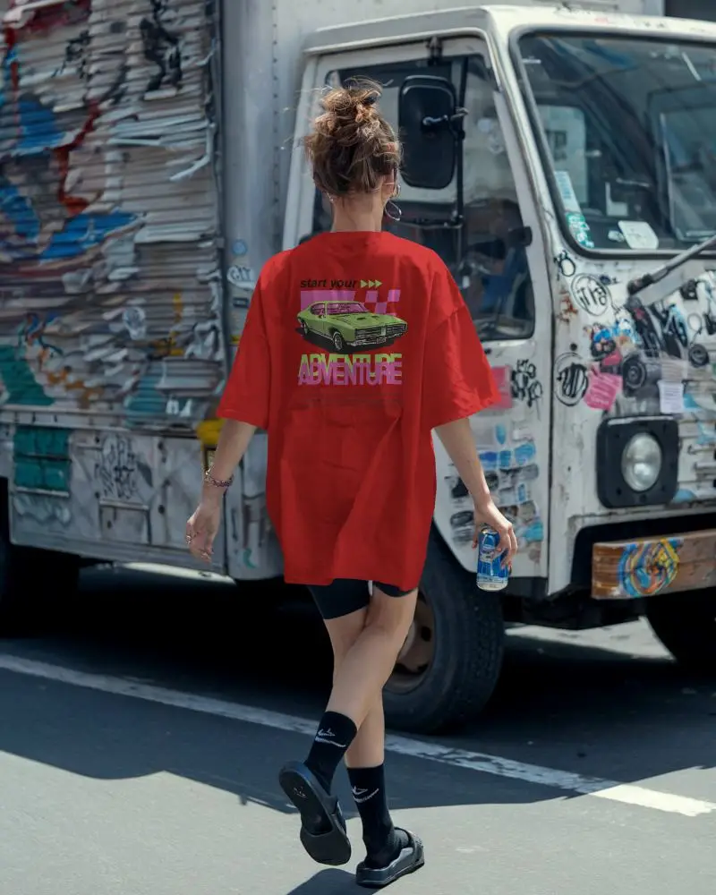 Urban Streetwear Boxy T Shirt Mockup Female Model Walking With Can In Hand In Front Of Graffiti Truck Edgy Casual Scene
