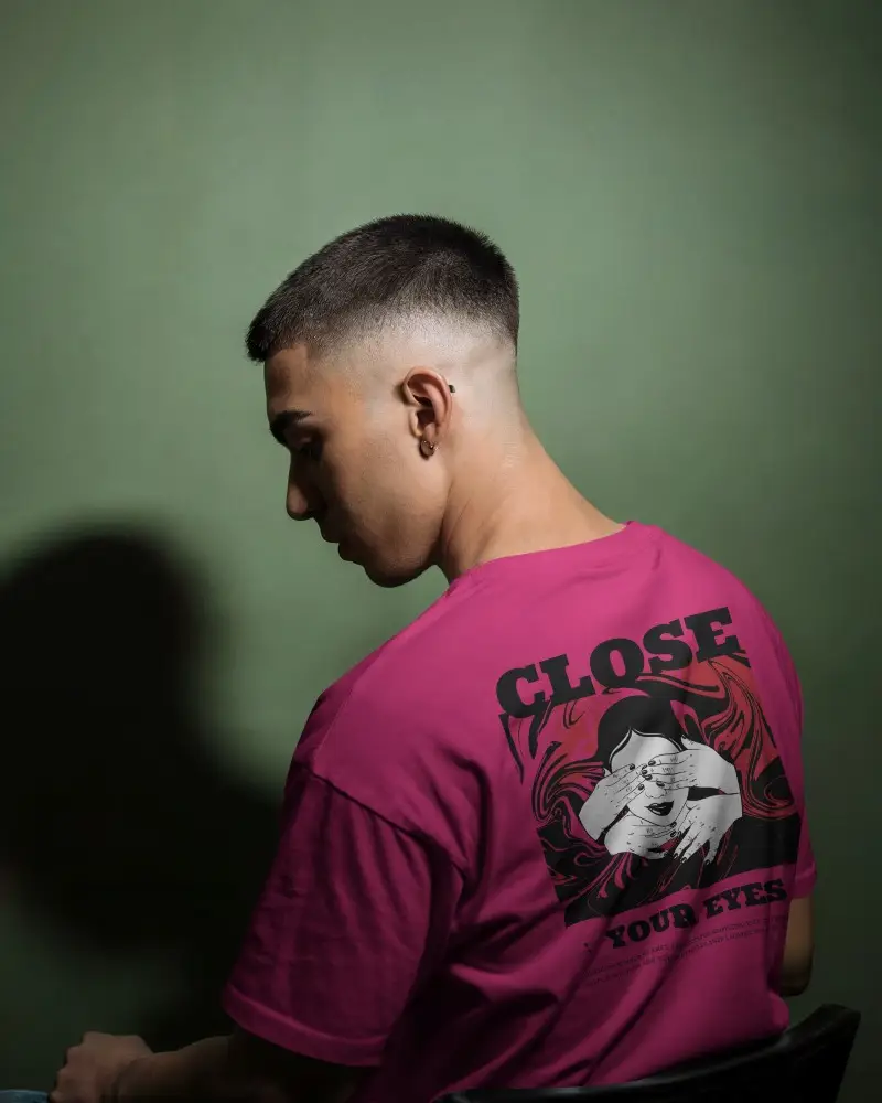 Studio Lit Tshirt Mockup Male Model Facing Away Sitting Against Olive Green Wall High Contrast Shadowed Look