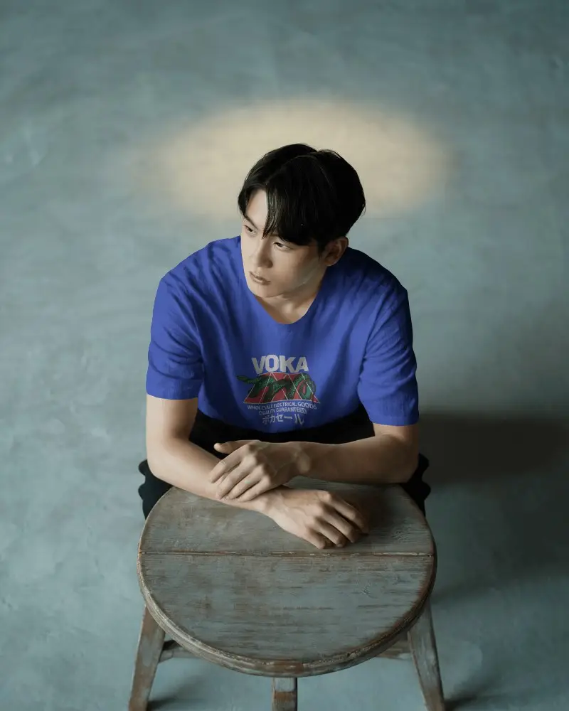 Moody Studio T Shirt Mockup Male Model Sitting On Wooden Stool Under Spotlight Minimal Background