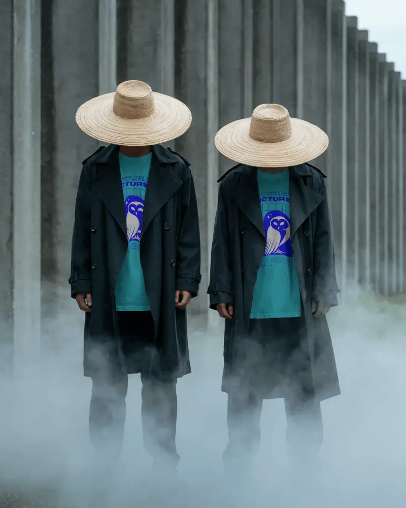 Twin Models Tshirt Mockup Wearing Straw Hats And Black Coats In Smoky Outdoor Industrial Setting