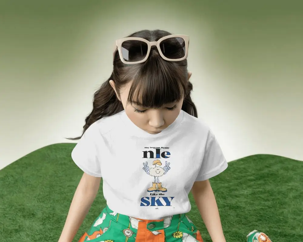 Kids Fashion Tshirt Mockup Girl Looking Down In Playful Studio Green Grass Inspired Backdrop