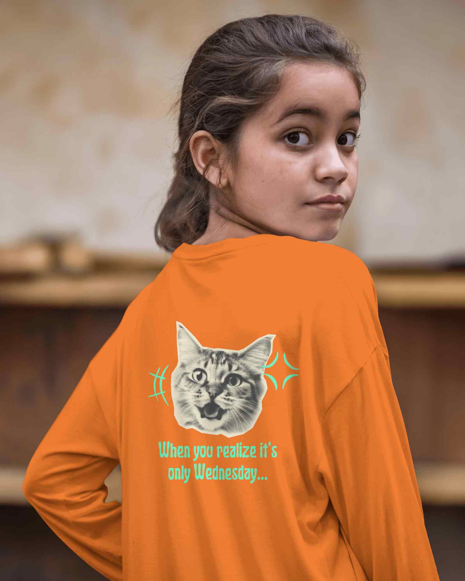 Playful Kid T Shirt Mockup Girl In Bright Orange Long Sleeve Tee With Funny Cat Print Looking Back Outdoor Rustic Background Casual And Fun Look