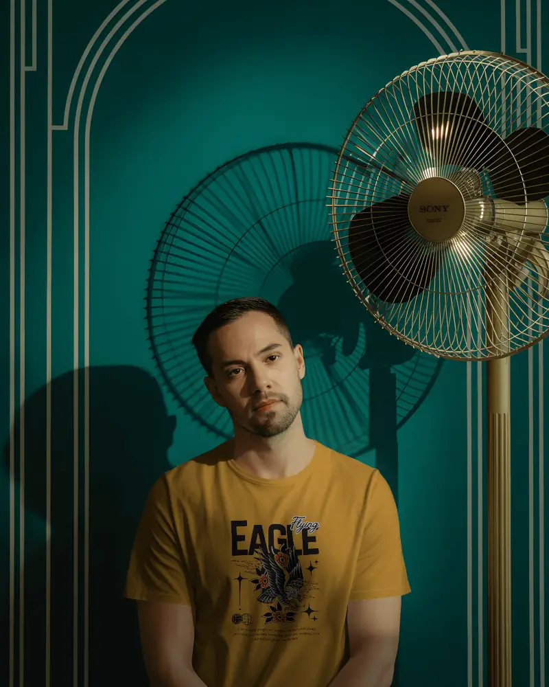 Moody Vintage Tshirt Mockup Male Model Standing In Retro Room With Electric Fan And Shadow Lines 02027