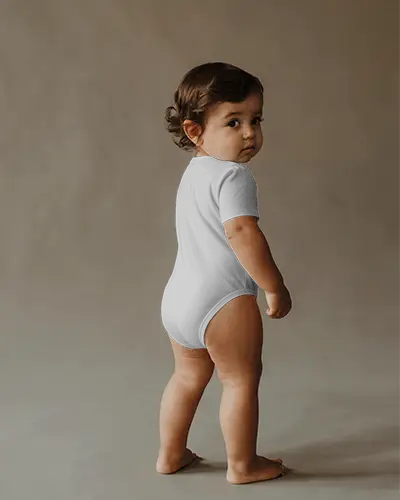 Cinematic Back Angle Onesie Mockup Toddler Turning Head In Soft Textured Studio Space