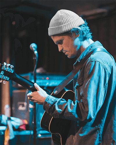 Moody Live Music Beanie Mockup Male Guitarist In Denim Jacket Under Blue Stage Lighting Intimate Concert Vibe