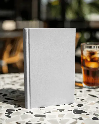 Hardcover Book Mockup On Terrazzo Cafe Table With Iced Drink In Bright Daylight
