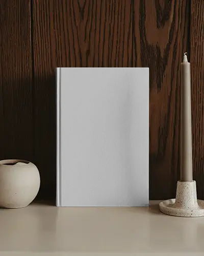 Hardcover Book Mockup On Cream Shelf With Ceramic Candle And Dark Wooden Wall Backdrop