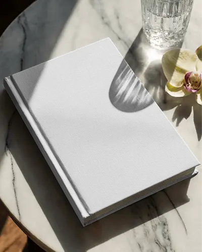 Angled Hardcover Book Mockup On White Marble Table With Glass Water And Orchid Flower