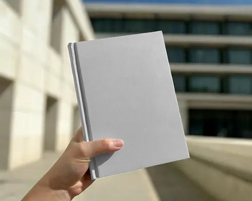 Hand Holding Book Mockup Outdoors With Modern Building In Sunny Daylight Background