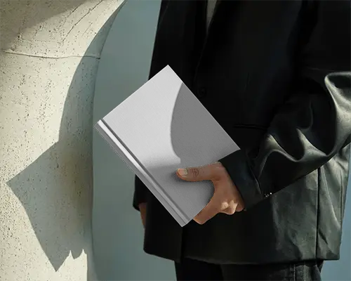 Person Holding Hardcover Book Mockup With Creased Pages Wearing Dark Coat Outdoor Shadows On Cover