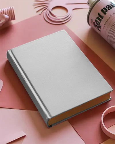 Hardcover Book Mockup Laying On Matte Surface With Art Supplies Around