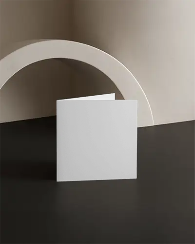Square Folded Brochure Mockup Standing On Black Surface Against Textured Arch Backdrop Soft Neutral Lighting Modern Minimal Promotional Display Scene