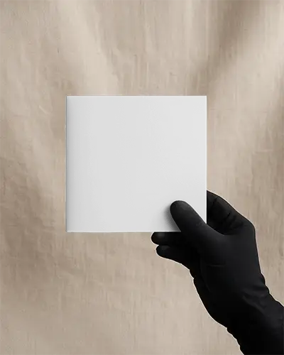 Hand Holding Square Brochure Mockup In Front Of Plain Fabric Backdrop Promotional Scene For Retail Discount Campaign Presentation