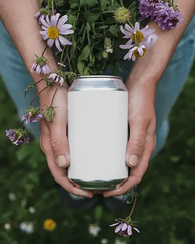 Person Holding Blank Can Mockup Surrounded By Nature Flowers And Greenery For Design