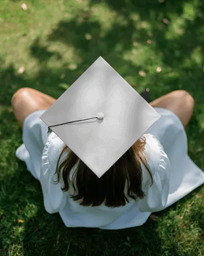 Graduation Cap Mockup On Student Sitting In Sunlit Grass From Top View